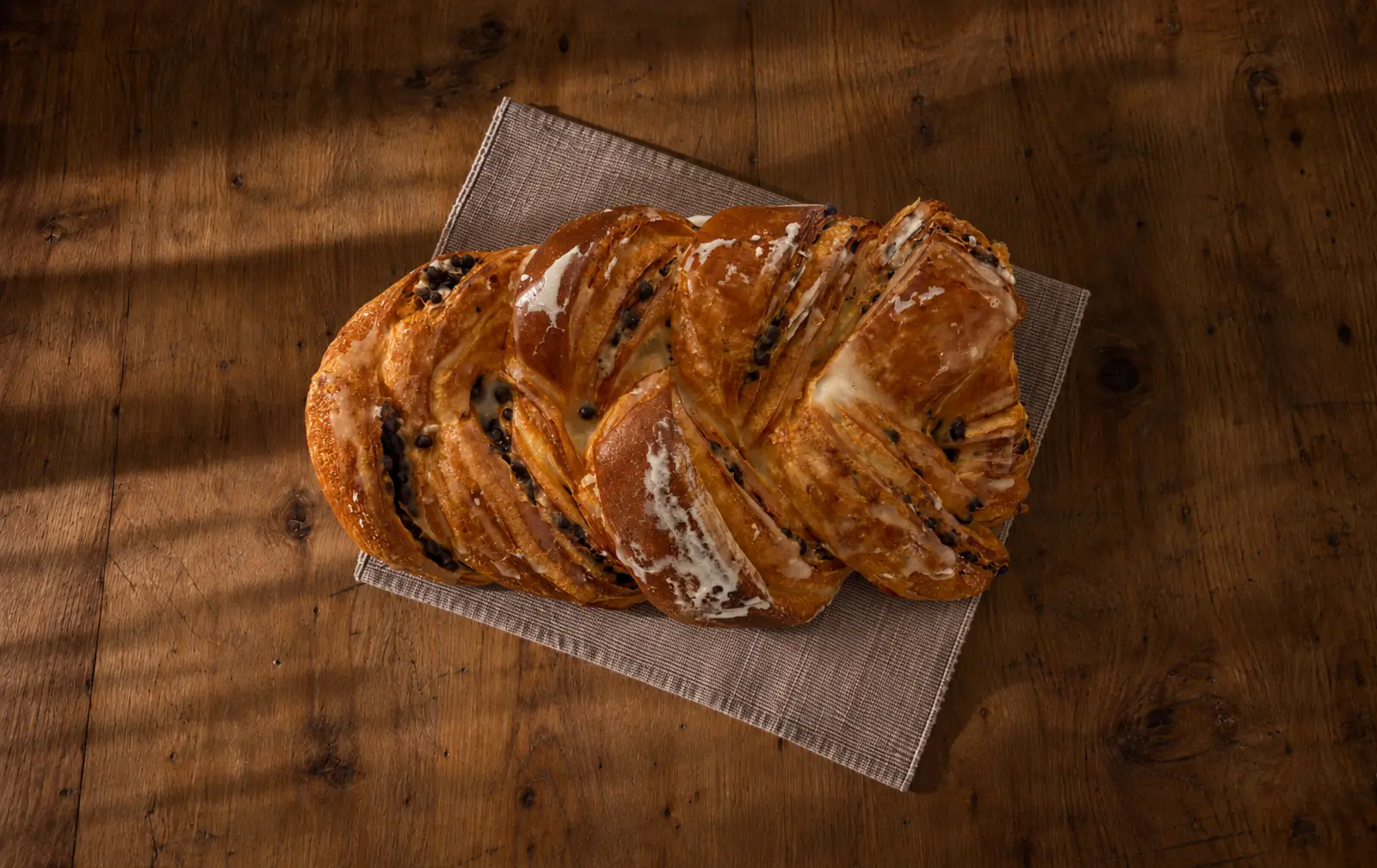 La nostra treccia sfogliata con gocce di cioccolato e un filo di glassa, su un tovagliolo su un tavolo di legno.