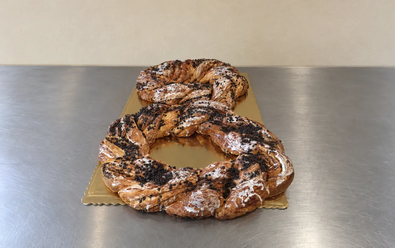 Un nostro treccione a forma di 8 con gocce di cioccolato e glassa, sul vassoio dorato, su un banco di acciaio.